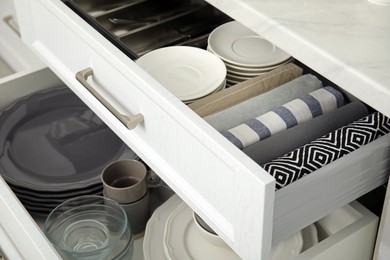 Photo of Open drawers of kitchen cabinet with different dishware and towels, closeup