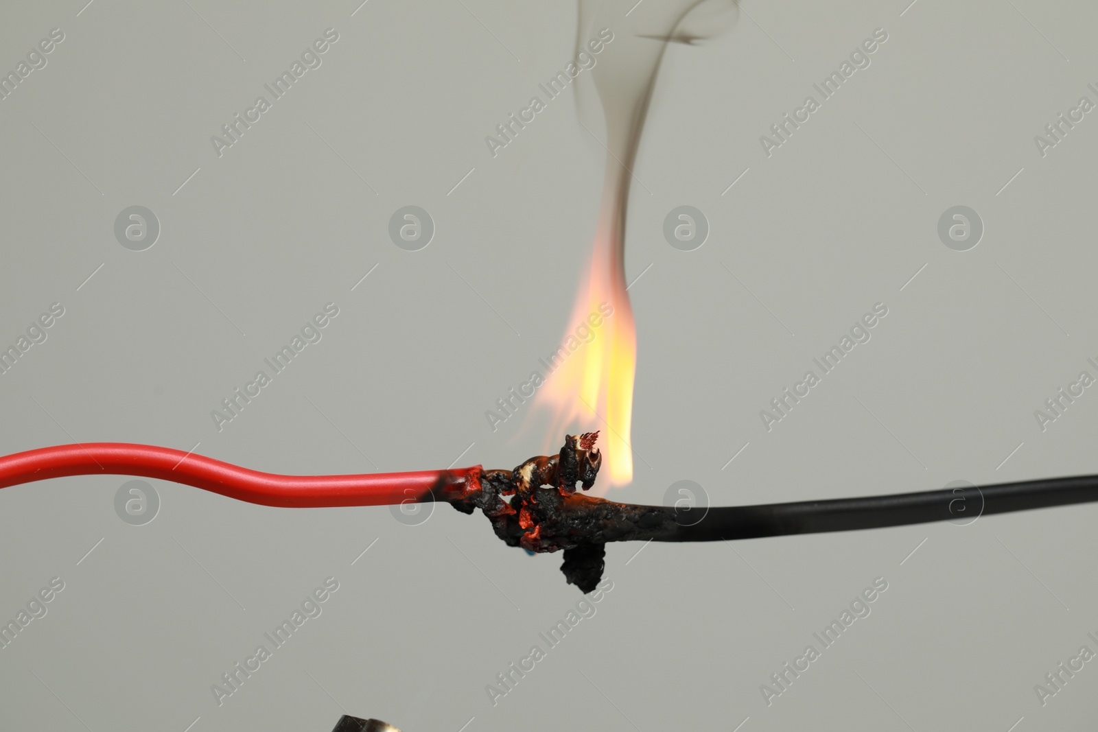 Photo of Inflamed red wire on grey background, closeup. Electrical short circuit