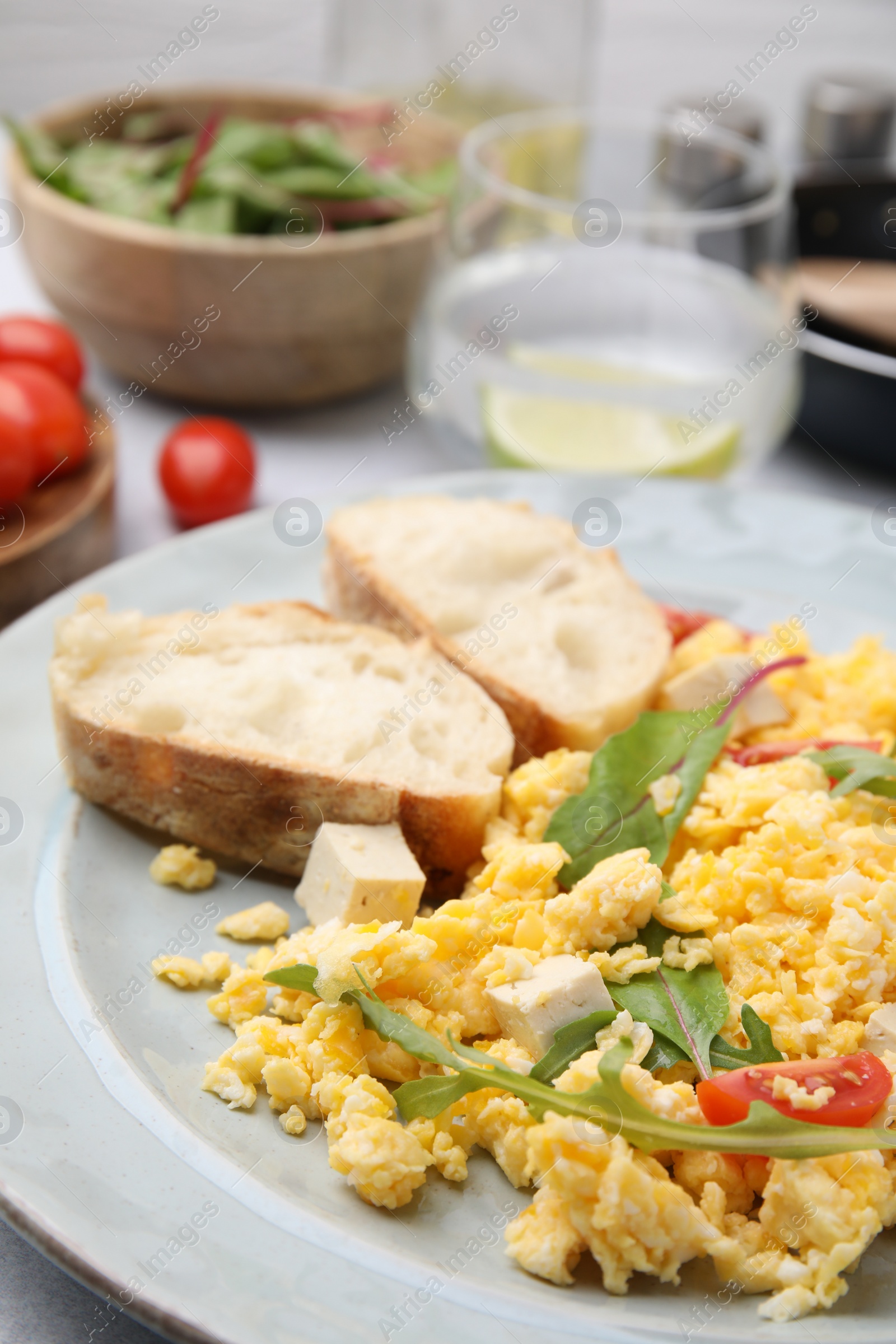 Photo of Plate with delicious scrambled eggs, tofu and slices of baguette on table, closeup