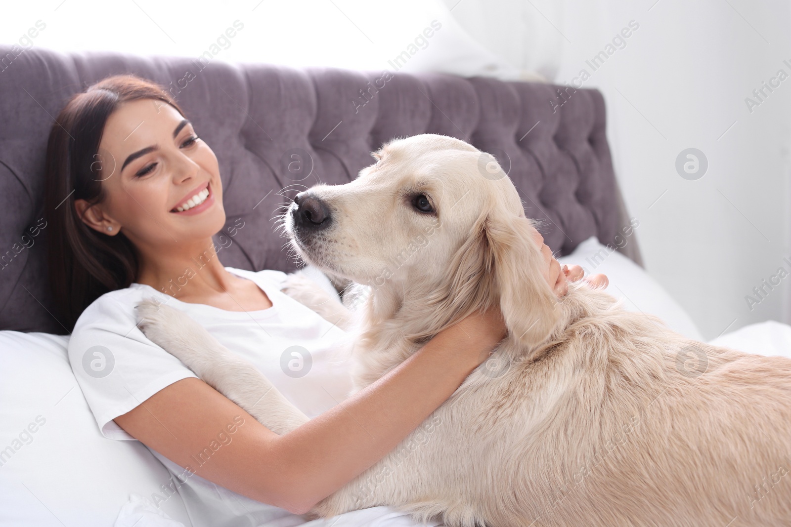 Photo of Young woman and her Golden Retriever dog on bed at home