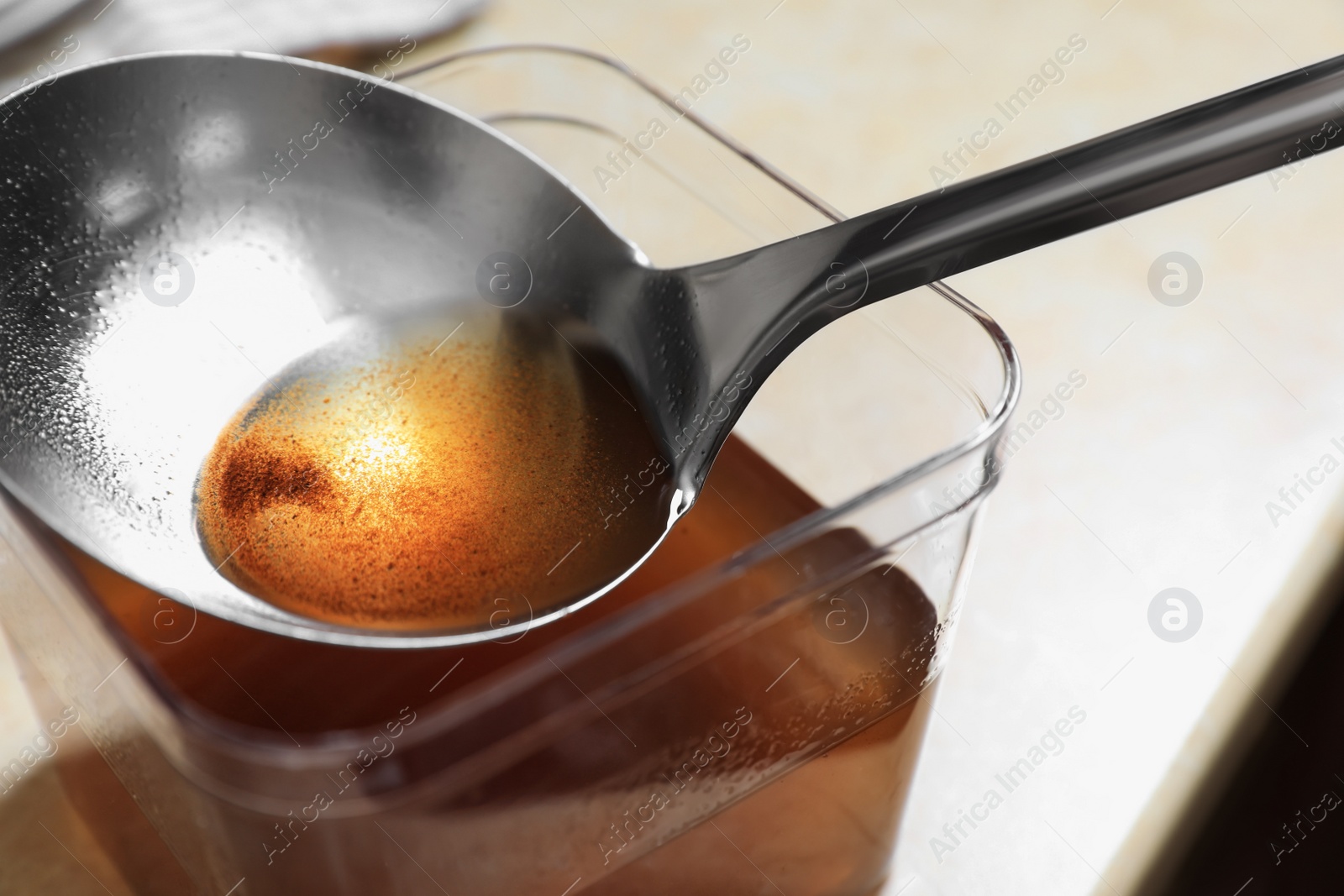 Photo of Container and ladle with used cooking oil on beige table, closeup