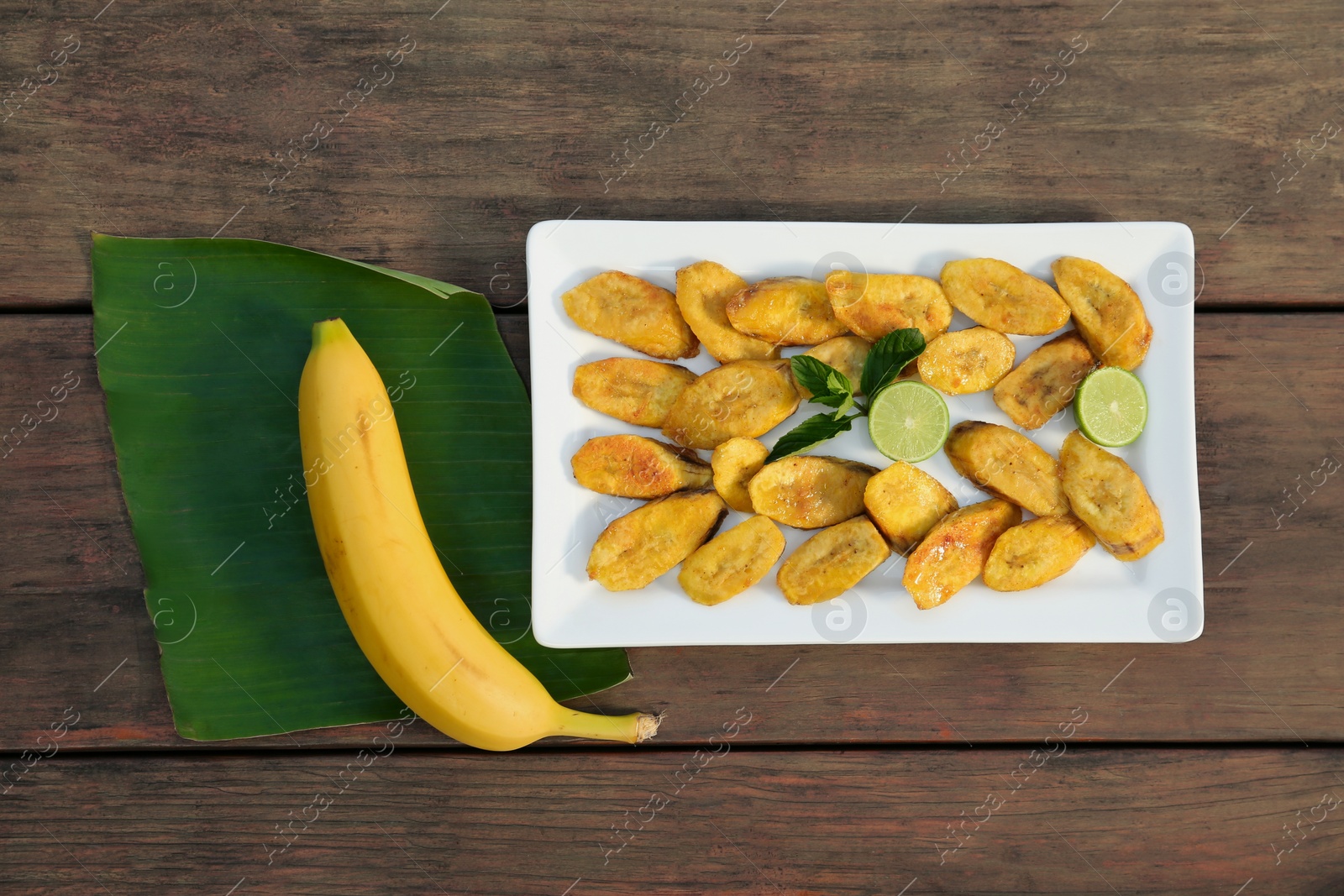 Photo of Tasty deep fried banana slices and fresh fruits on wooden table, flat lay