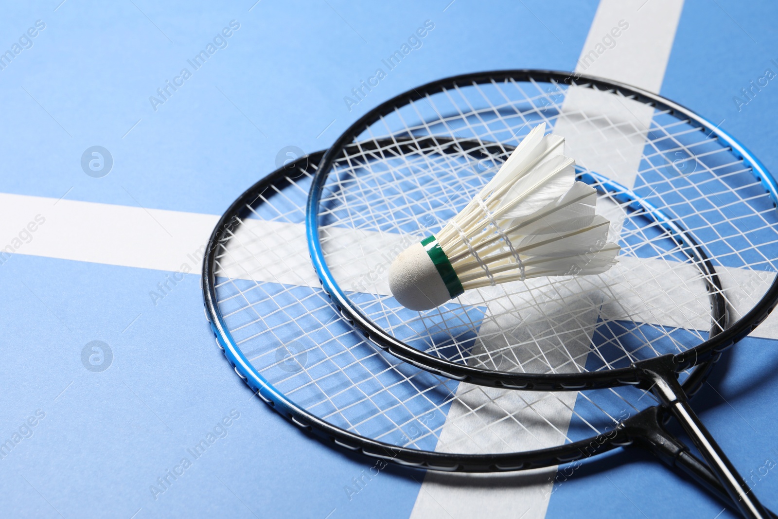 Photo of Feather badminton shuttlecock and rackets on blue background, closeup. Space for text