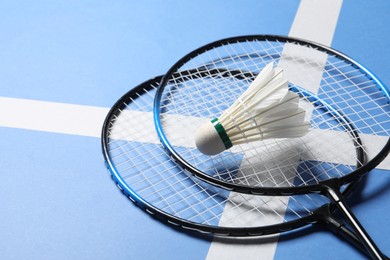 Feather badminton shuttlecock and rackets on blue background, closeup. Space for text