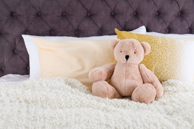 Photo of Cute teddy bear sitting on bed indoors. Space for text