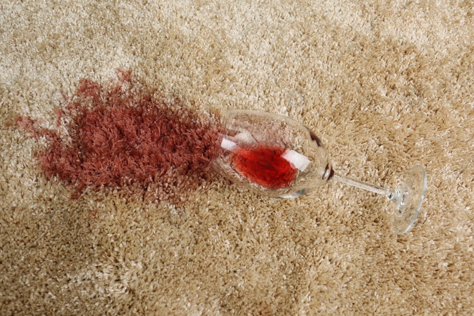 Photo of Overturned glass and spilled red wine on soft carpet, top view