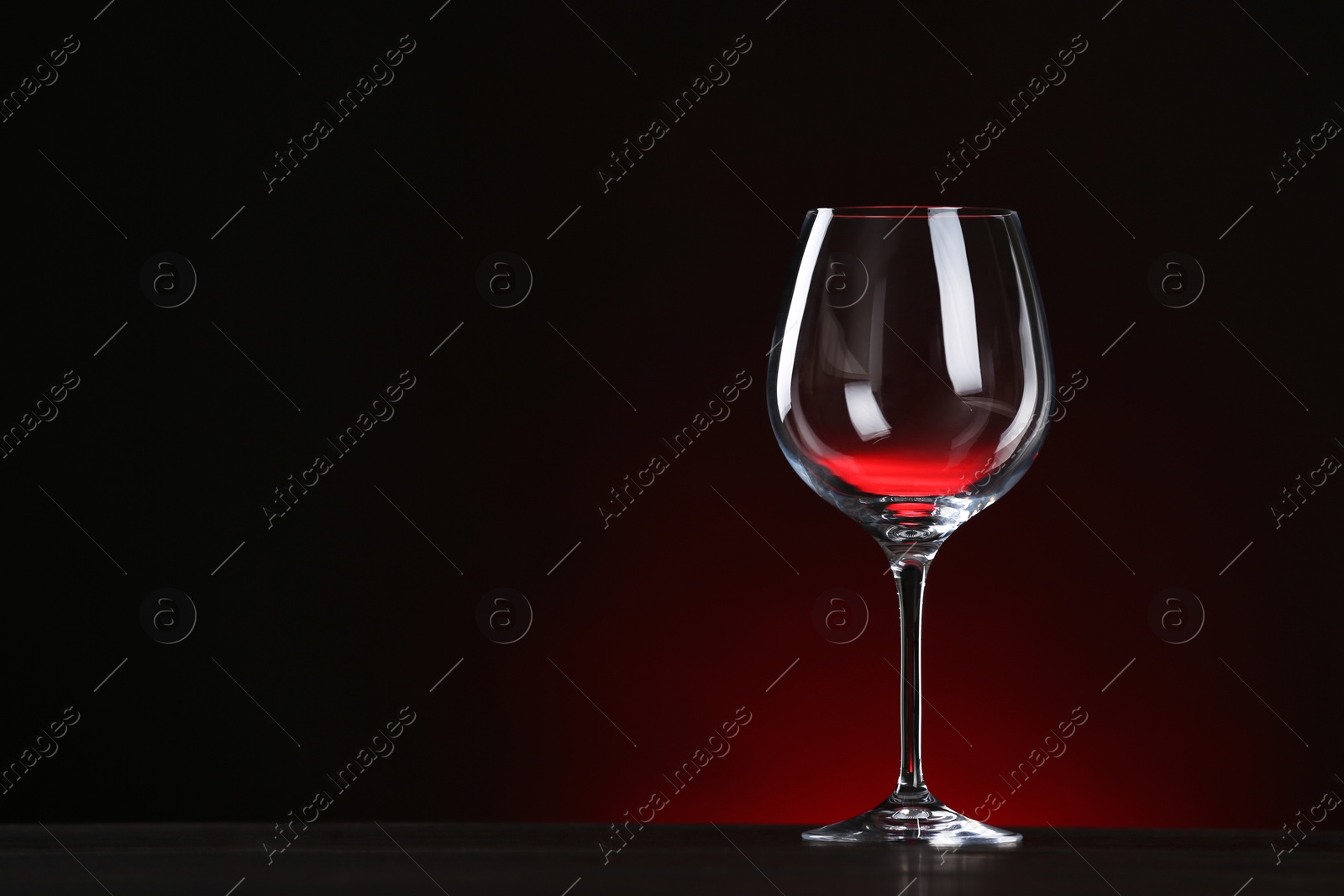 Photo of Empty wine glass on table against dark background, space for text