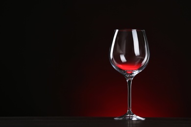Photo of Empty wine glass on table against dark background, space for text