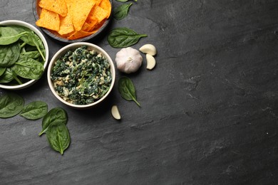 Photo of Tasty spinach dip with egg in bowl, garlic and nachos chips on black table, flat lay. Space for text