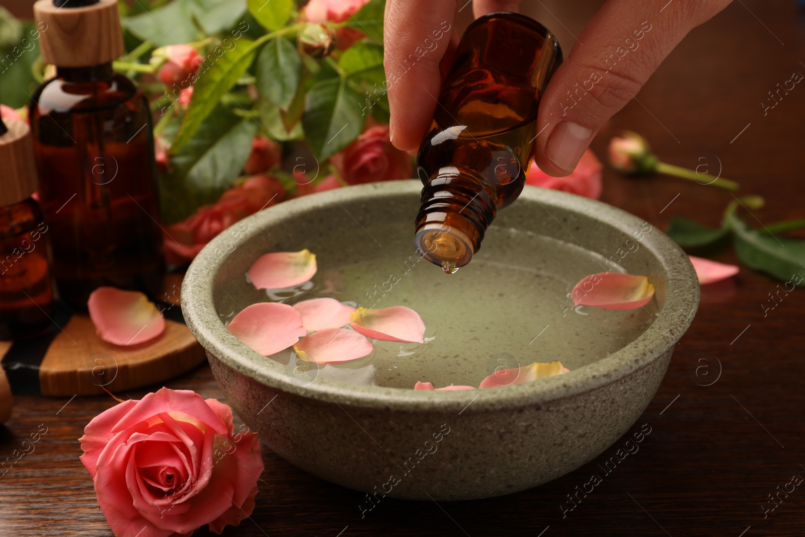 Photo of Woman dripping essential oil into bowl at wooden table, closeup. Aromatherapy treatment