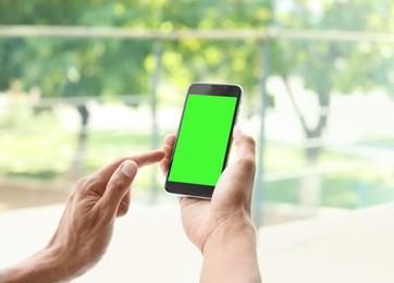 Man using smartphone with green screen on blurred background, closeup. Gadget display with chroma key. Mockup for design