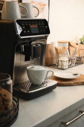 Photo of Modern coffee machine with cup of cappuccino in kitchen