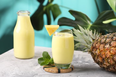 Photo of Tasty pineapple smoothie, mint and fruit on grey textured table