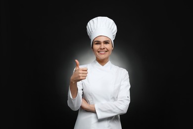 Photo of Happy female chef showing thumbs up on black background