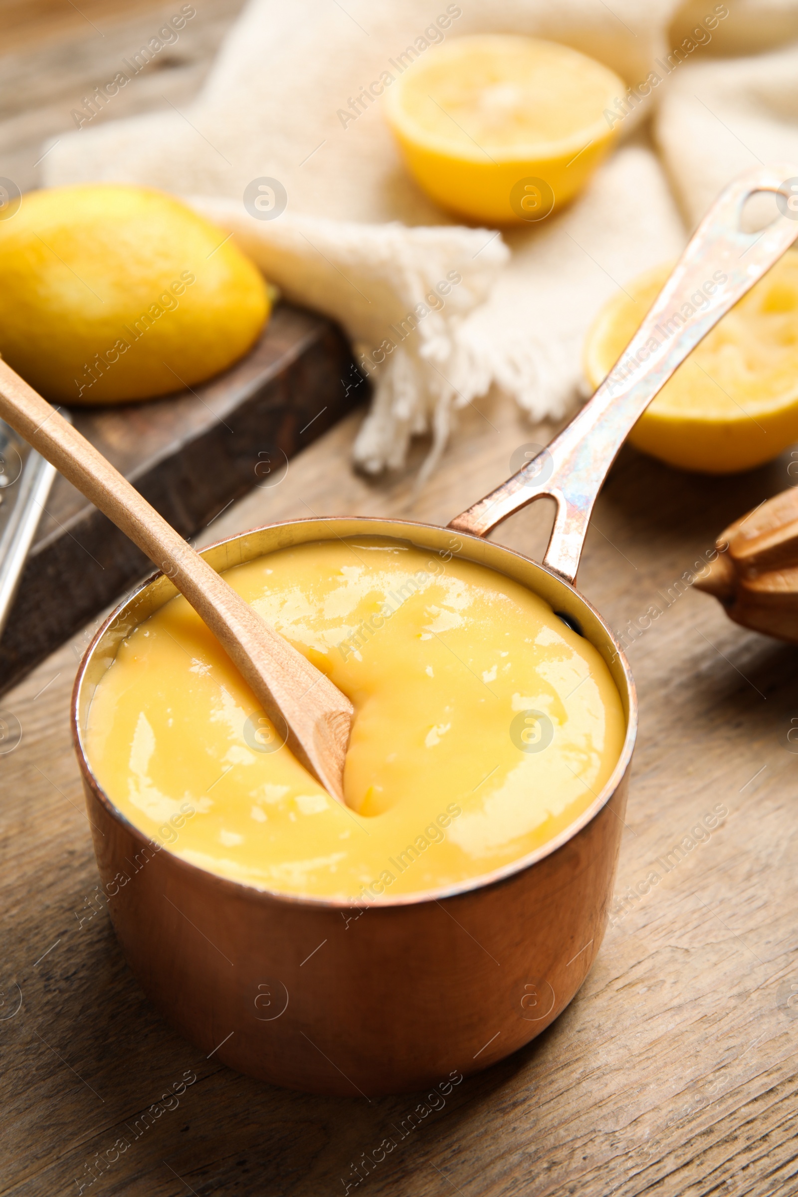 Photo of Delicious lemon curd in saucepan on wooden table