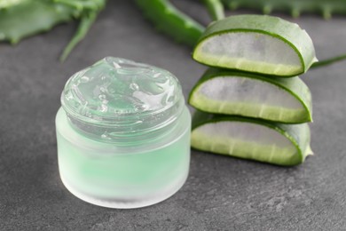 Jar of natural gel and sliced aloe vera leaves on grey table, closeup