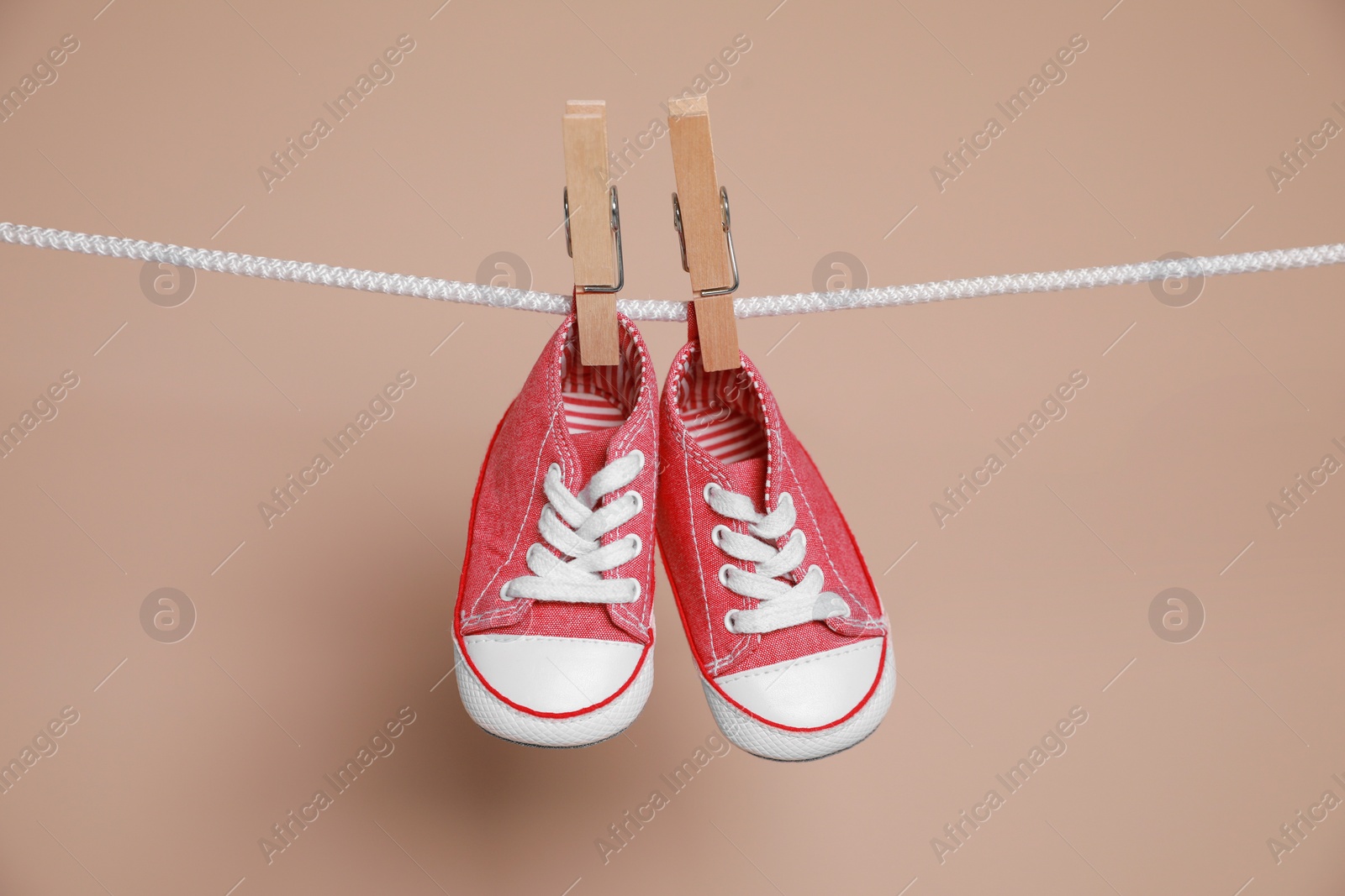 Photo of Cute small baby shoes hanging on washing line against brown background