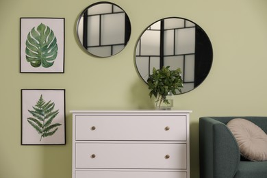 Photo of White chest of drawers with lamp and mirrors on wall in living room. Interior design