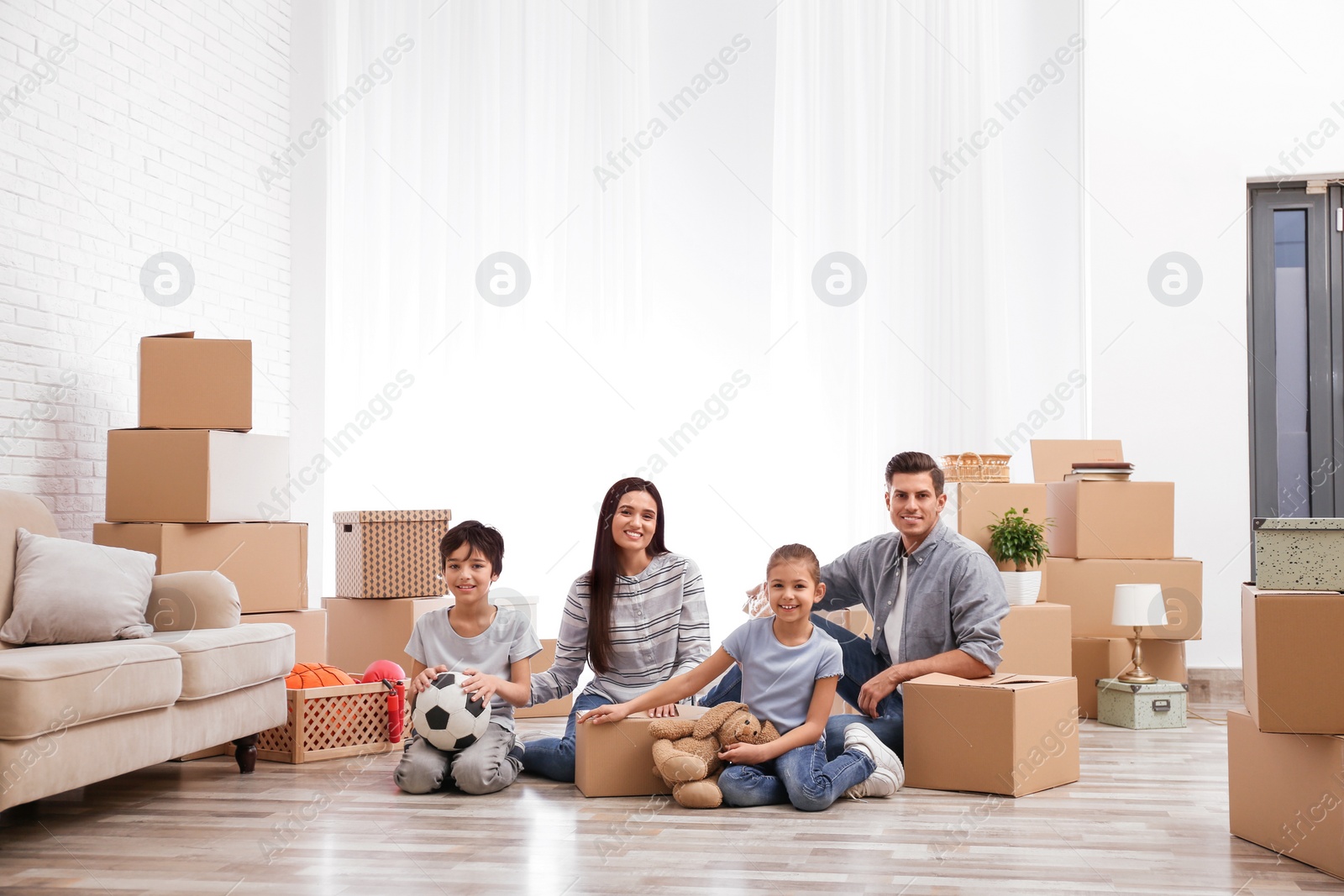 Photo of Happy family in room with cardboard boxes on moving day