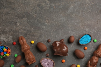 Photo of Flat lay composition with chocolate Easter bunnies, eggs and candies on grey table. Space for text