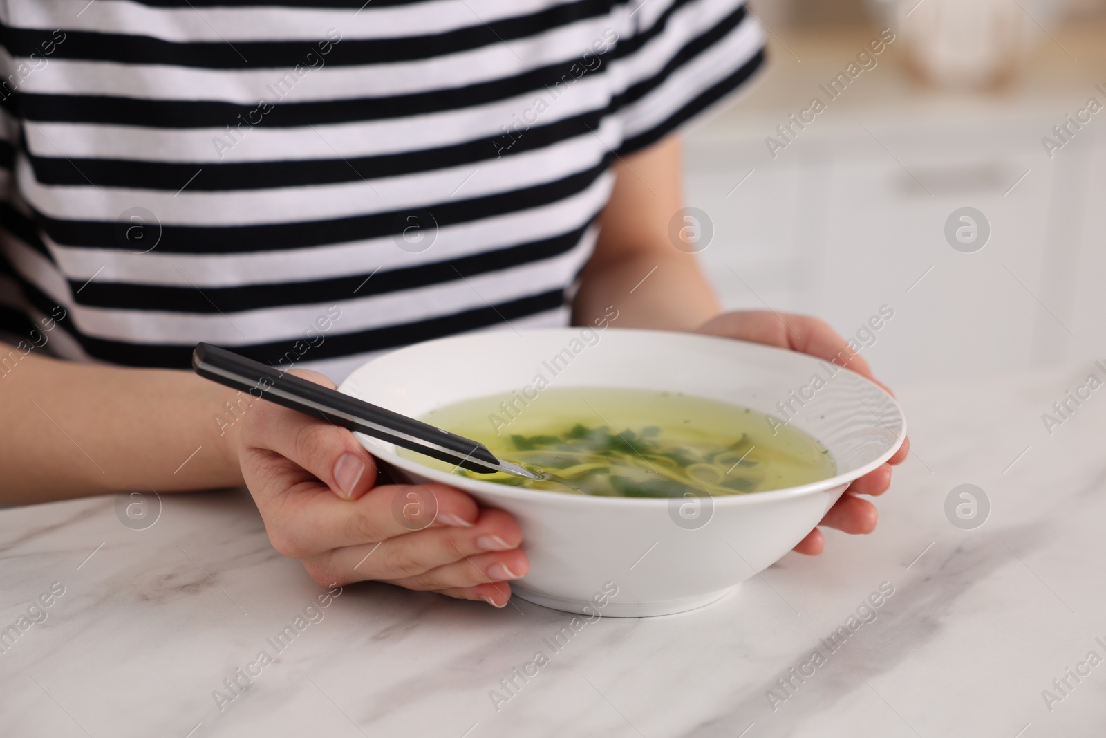 Photo of Woman with bowl of tasty soup at white marble table, closeup