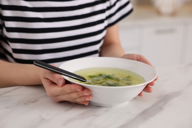 Woman with bowl of tasty soup at white marble table, closeup