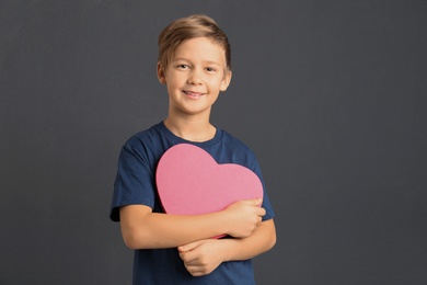 Cute boy holding heart shaped box on grey background