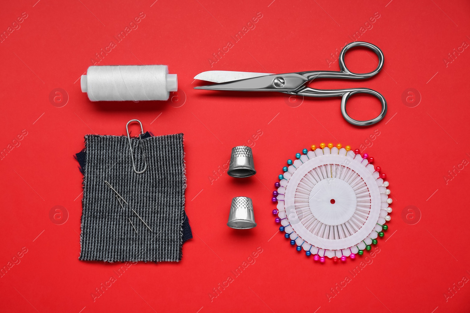 Photo of Flat lay composition with thimbles and different sewing tools on red background