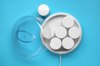 Modern yogurt maker with jars on light blue background, flat lay