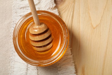Photo of Dipper and honey in jar on wooden table, top view. Space for text