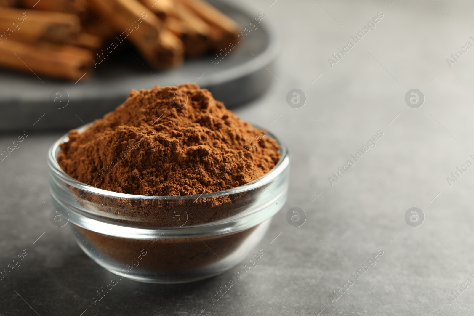 Photo of Bowl of cinnamon powder on grey table, closeup. Space for text