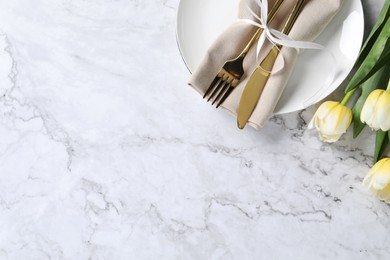 Stylish table setting with cutlery and tulips on white marble background, flat lay. Space for text