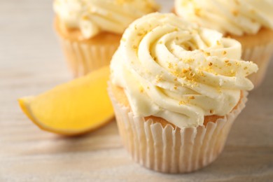 Photo of Tasty cupcakes with cream, zest and lemon slice on light wooden table, closeup