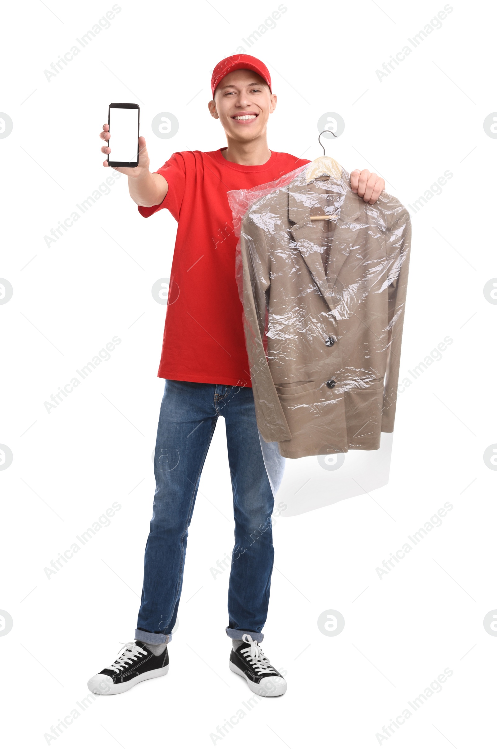 Photo of Dry-cleaning delivery. Happy courier holding jacket in plastic bag and smartphone on white background