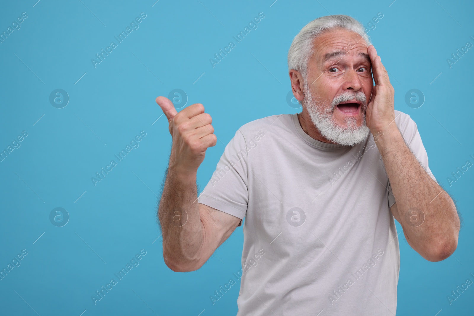 Photo of Special promotion. Emotional senior man pointing at something on light blue background. Space for text