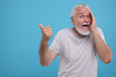 Photo of Special promotion. Emotional senior man pointing at something on light blue background. Space for text