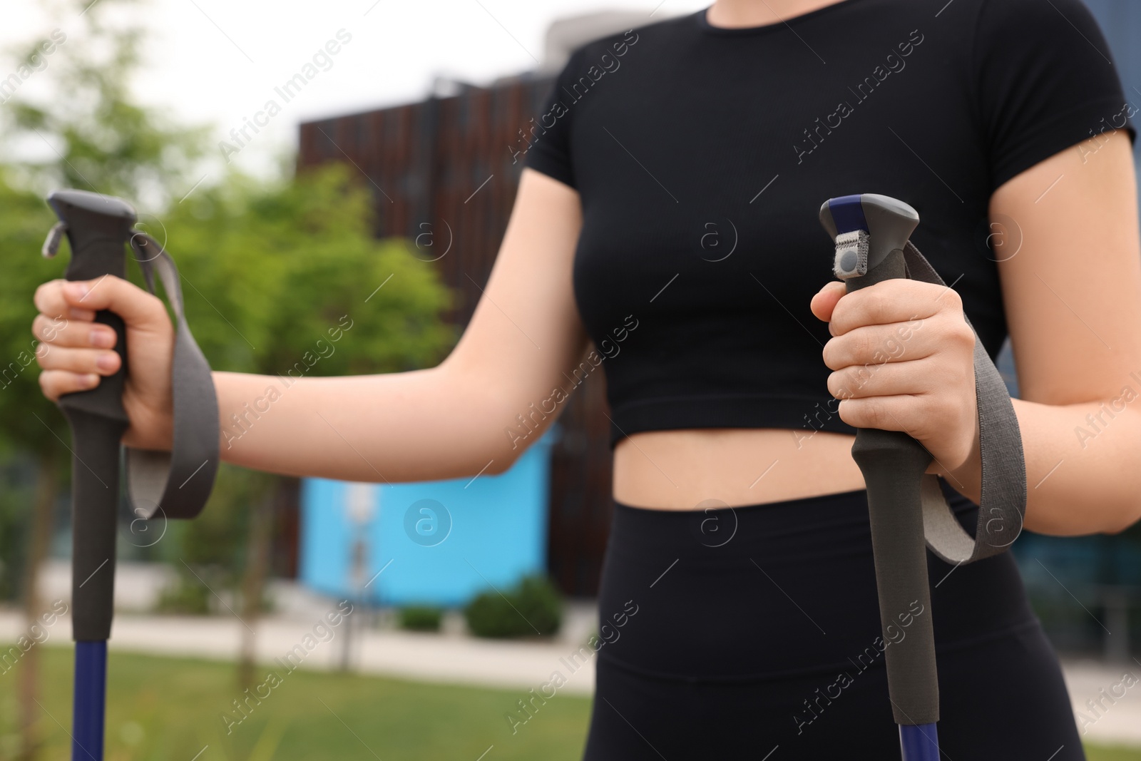 Photo of Young woman practicing Nordic walking with poles outdoors, closeup