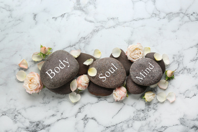 Photo of Stones with words MIND, BODY, SOUL and rose flowers on marble background, flat lay. Zen lifestyle