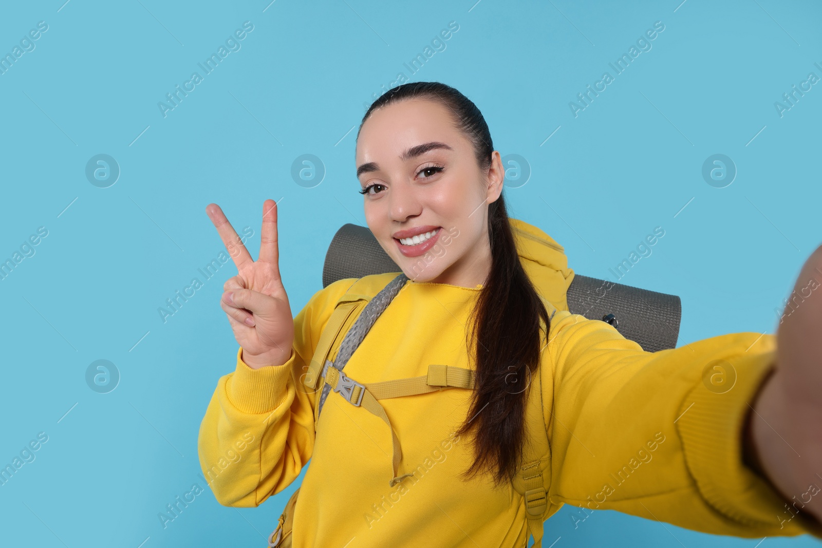 Photo of Smiling young woman with backpack taking selfie on light blue background. Active tourism