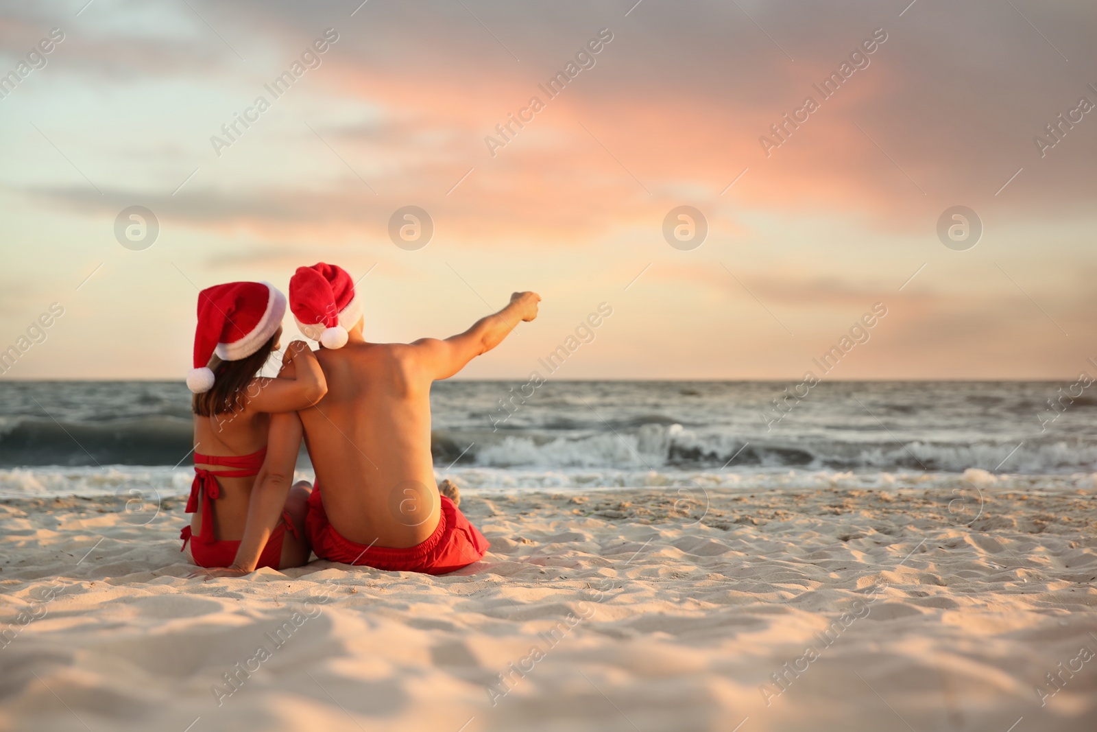 Photo of Lovely couple with Santa hats together on beach, back view. Christmas vacation