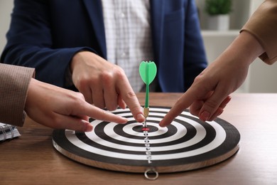 Business targeting concept. People pointing at dartboard at wooden table indoors, closeup