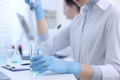 Scientist dripping sample into beaker in laboratory, closeup