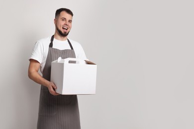 Happy professional confectioner in apron holding cake box indoors. Space for text