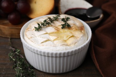 Photo of Tasty baked camembert and thyme in bowl on wooden table, closeup