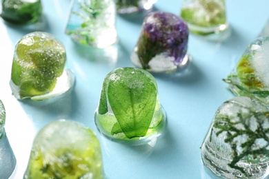 Ice cubes with flowers and leaves on light blue background