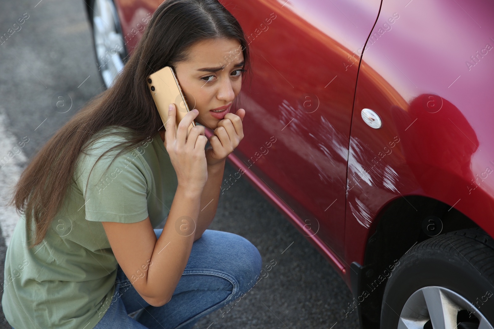 Photo of Stressed woman talking on phone near car with scratch outdoors