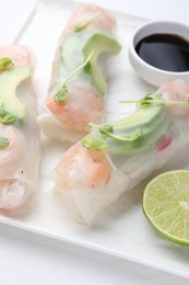 Delicious spring rolls, lime and soy sauce on white wooden table, closeup