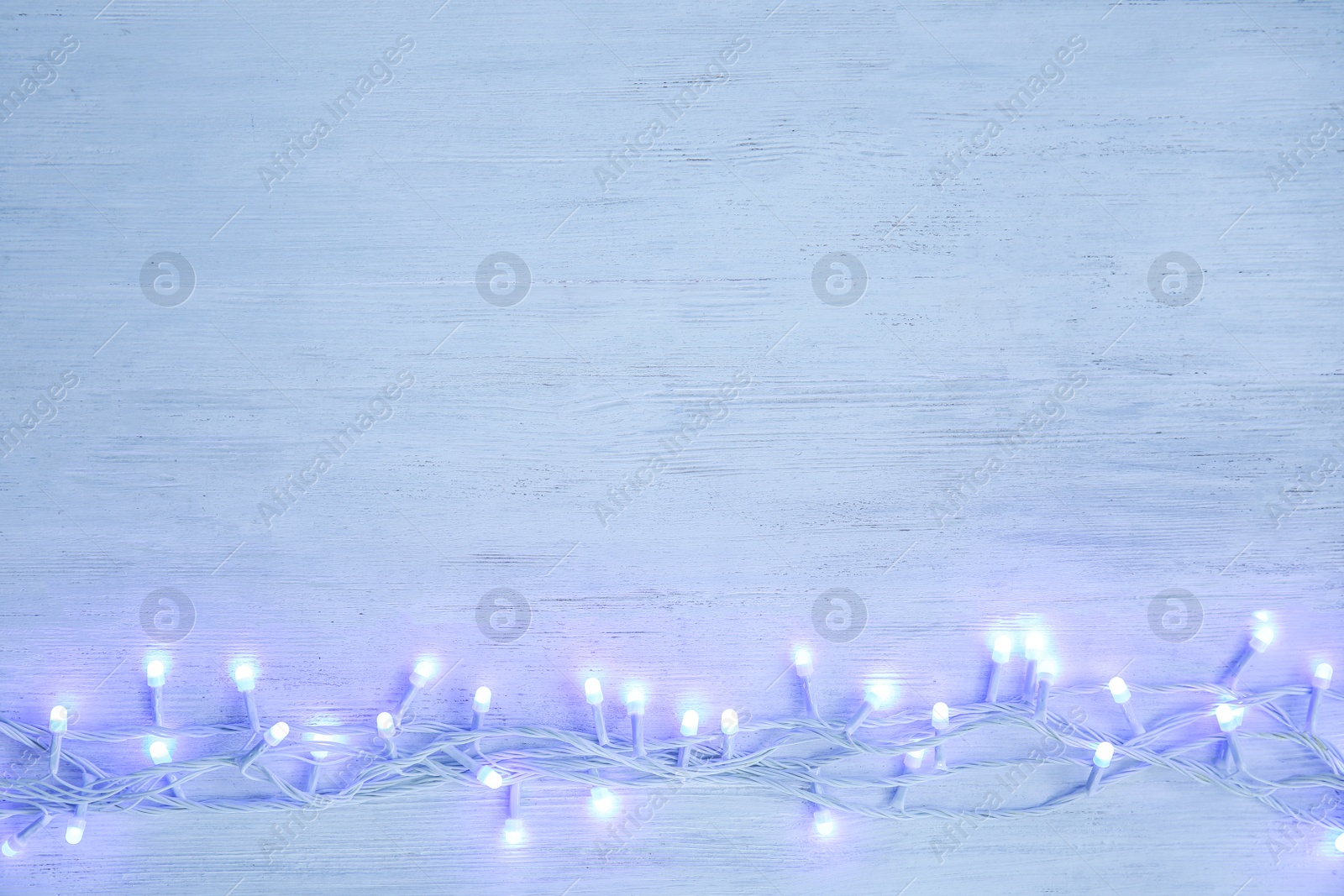 Photo of Glowing Christmas lights on wooden background, top view