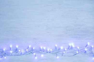 Photo of Glowing Christmas lights on wooden background, top view