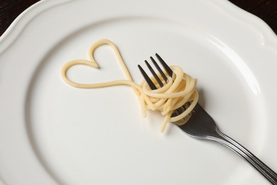 Photo of Heart made of tasty spaghetti and fork on table, closeup